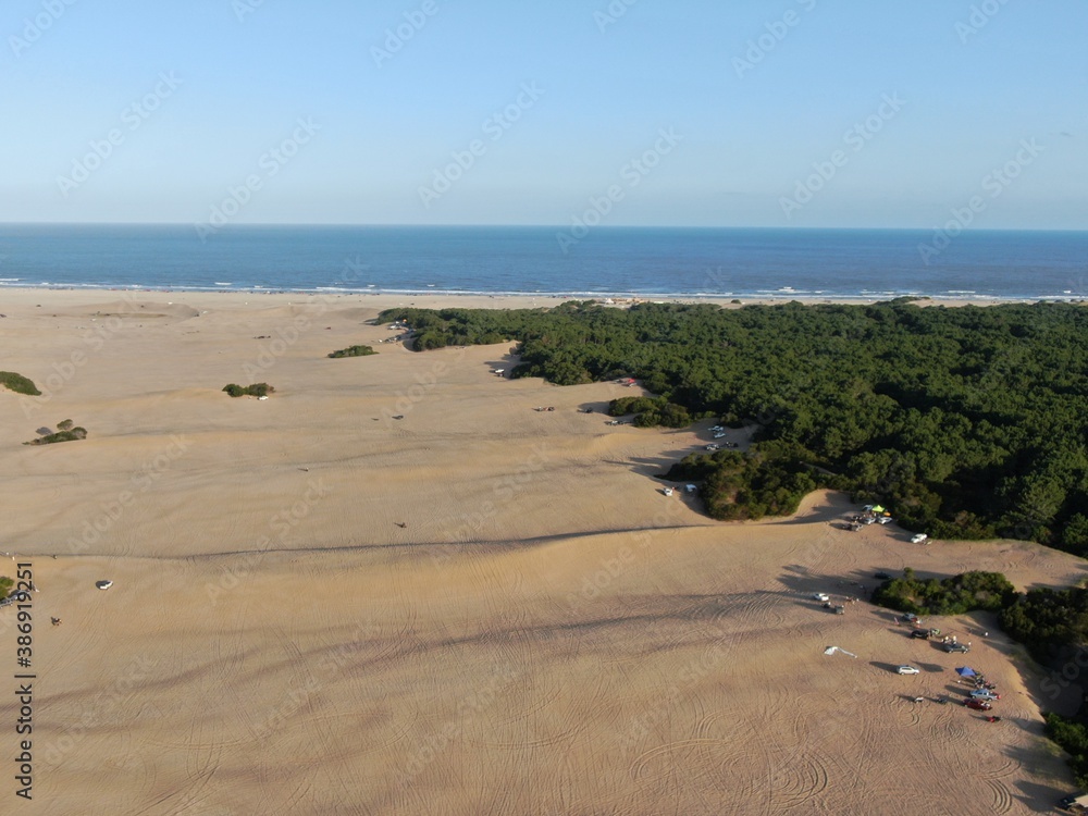 Vista aérea de las dunas cerca del mar, con algo de vegetación a la derecha, durante el atardecer.