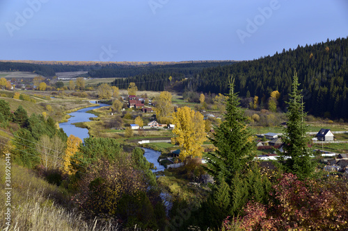 A small Ural village on the bank of a small clean river among the autumn landscape. In the foothills of the Western Urals, golden autumn.