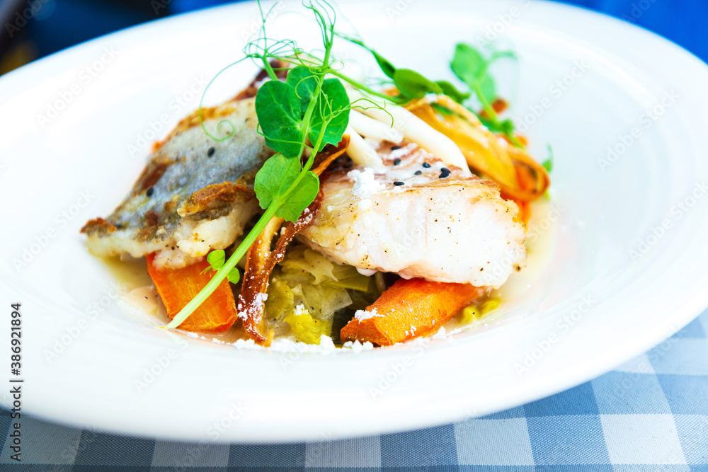 Delicious fillet of cod fish with carrots, leeks and mushrooms in white plate ready to be served