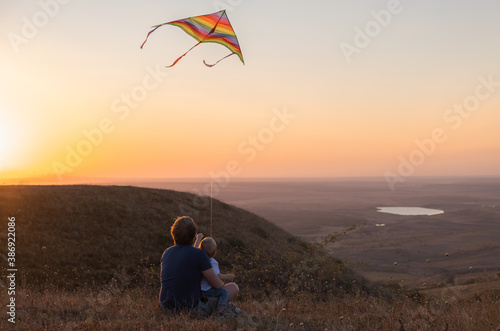 dad and baby boy fly a kite at sunset.