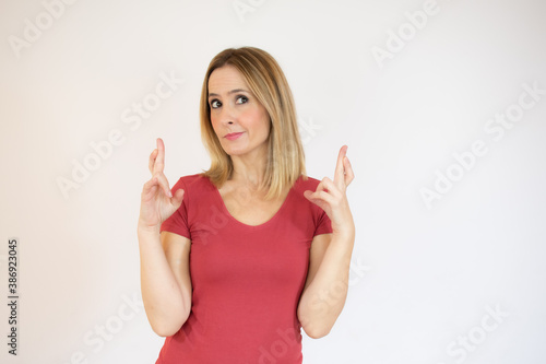 Portrait of a young woman standing over white background  holding fingers crossed for good luck