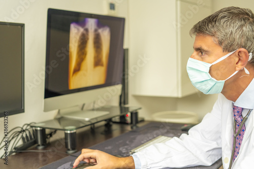 Male doctor wearing mask in covid-19 department looking at patient x-ray on the computer screen