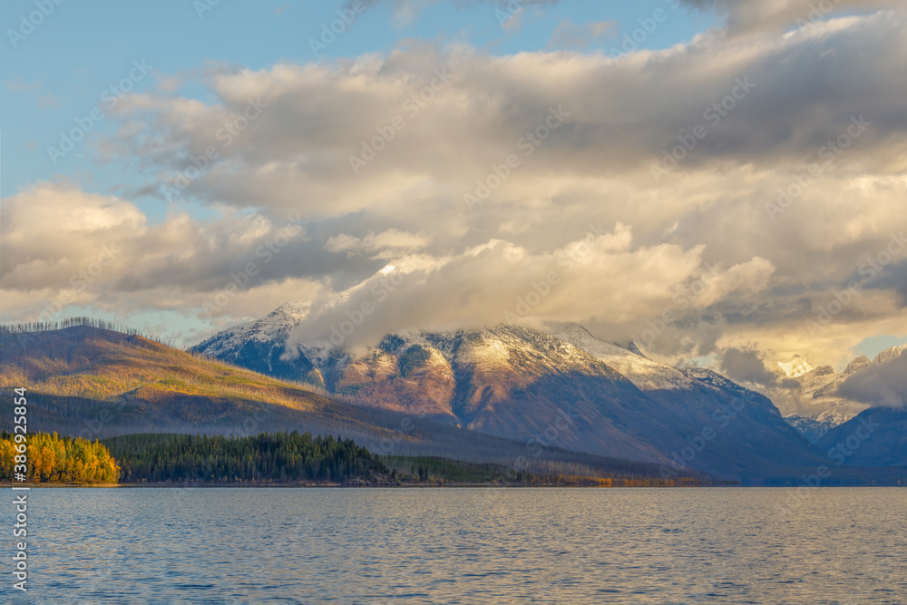 autumn landscape of majestic cloud enshrouded mountain in early morning with Lake McDonald in foreground, Glacier National Park, Montana
