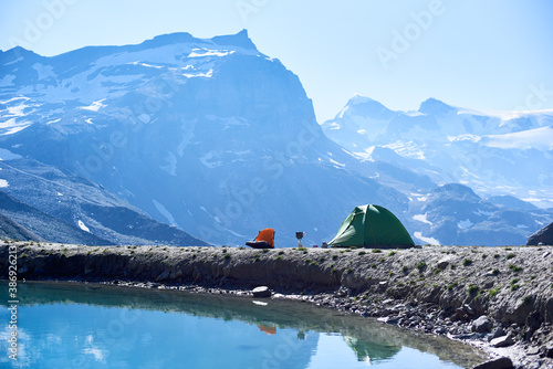 Beautiful landscape of blue lake and tourist tent in mountain valley. Majestic rocky hills and camp tent reflecting in crystal water. Concept of travelling, tourism camping and beauty of nature.