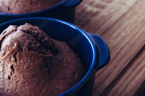 Delicious baked chocolate muffins in blue ceramic tins on wooden background. Side view. Close up