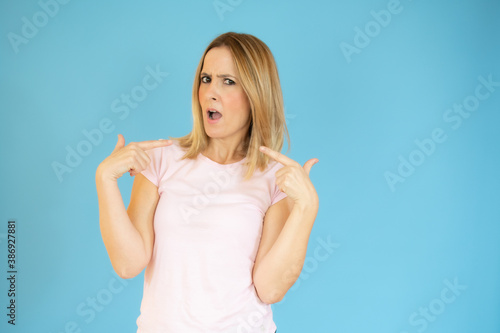 Portrait of young smiling woman in casual t-shirt pointing fingers herself isolated over blue background