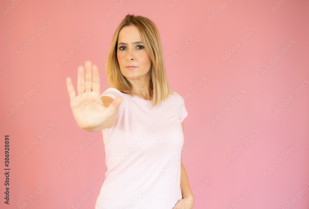 Young beautiful woman wearing casual t-shirt over pink background doing stop sing with palm of the hand. Warning expression with negative and serious gesture on the face. Young beautiful woman wearing casual t-shirt over pink background doing stop sing with palm of the hand. Warning expression with negative and serious gesture on the face.