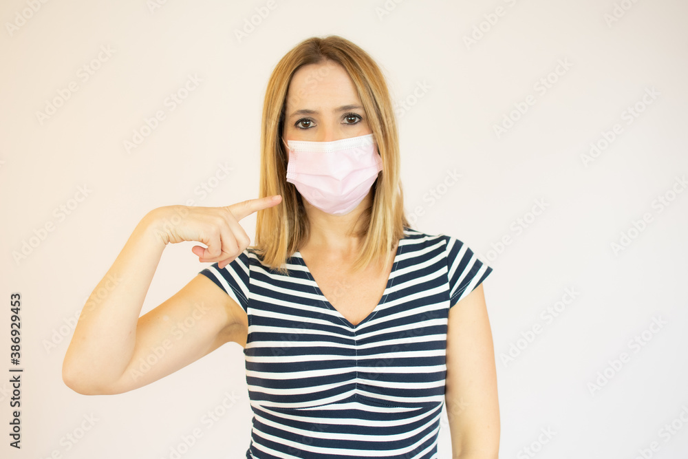 Caucasian woman wearing a face mask and pointing at it in a studio with a white background Caucasian woman wearing a face mask and pointing at it in a studio with a white background