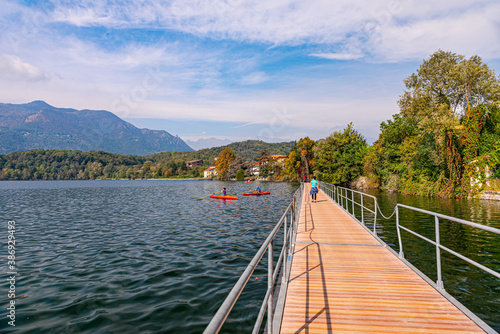 Avigliana, Italy. October 10th, 2020. Woman walks on the jetty of the lake in a autumn day, while other people are doing canoeing.