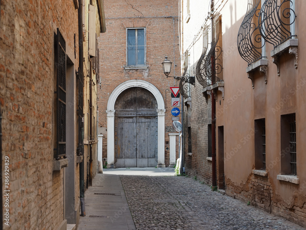 Ferrara, Italy. Cobbled street in the old town. There is an old house with a large wooden door.