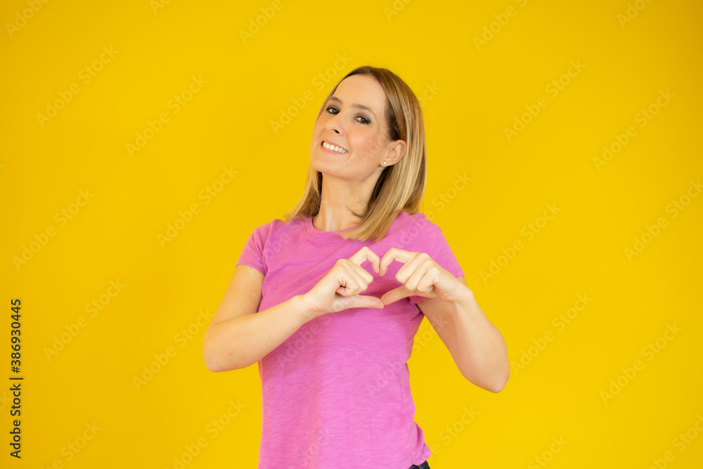 Young beautiful casual woman over yellow background smiling in love showing heart symbol and shape with hands. Romantic concept. Young beautiful casual woman over yellow background smiling in love showing heart symbol and shape with hands. Romantic concept.