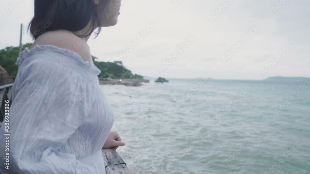 Slow motion Asian short hair woman touch wooden bridge on beach blue sea summer on cloudy sky. Relax happy female wear white dress travel after quarantine coronavirus with new normal social distancing Slow motion Asian short hair woman touch wooden bridge on beach blue sea summer on cloudy sky. Relax happy female wear white dress travel after quarantine coronavirus with new normal social distancing