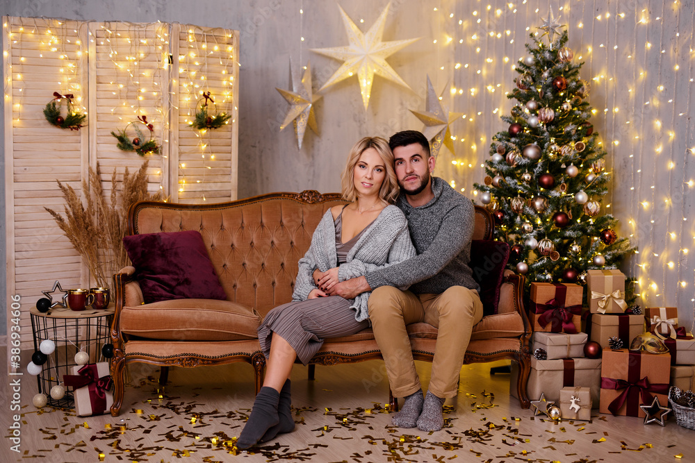 Obraz premium winter holidays and relationship concept - happy young couple in living room with decorated Christmas tree