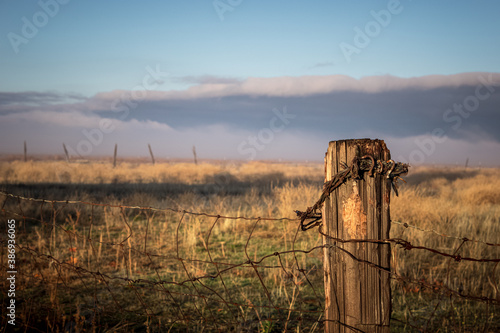 Fence post with barbed wire in valley with storm