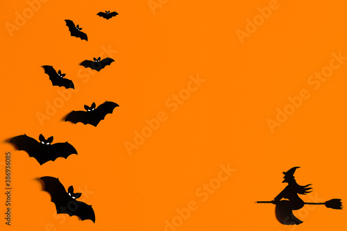 Silhouettes of a flock of bats and a witch flying on a broom made of black paper on an orange background. Halloween greeting template with copy space. Flat lay for your design. ready-made template