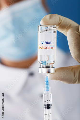 An ampoule with the inscription Virus Vaccine and a syringe in the hands of a scientist doctor in rubber gloves with a vaccine close-up.