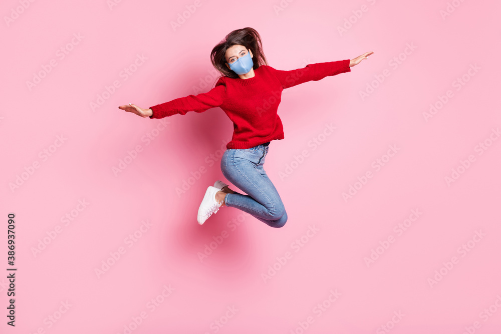 Full length portrait of girl jumping high wearing mask casual clothes keeping hands like plane isolated on pink color background