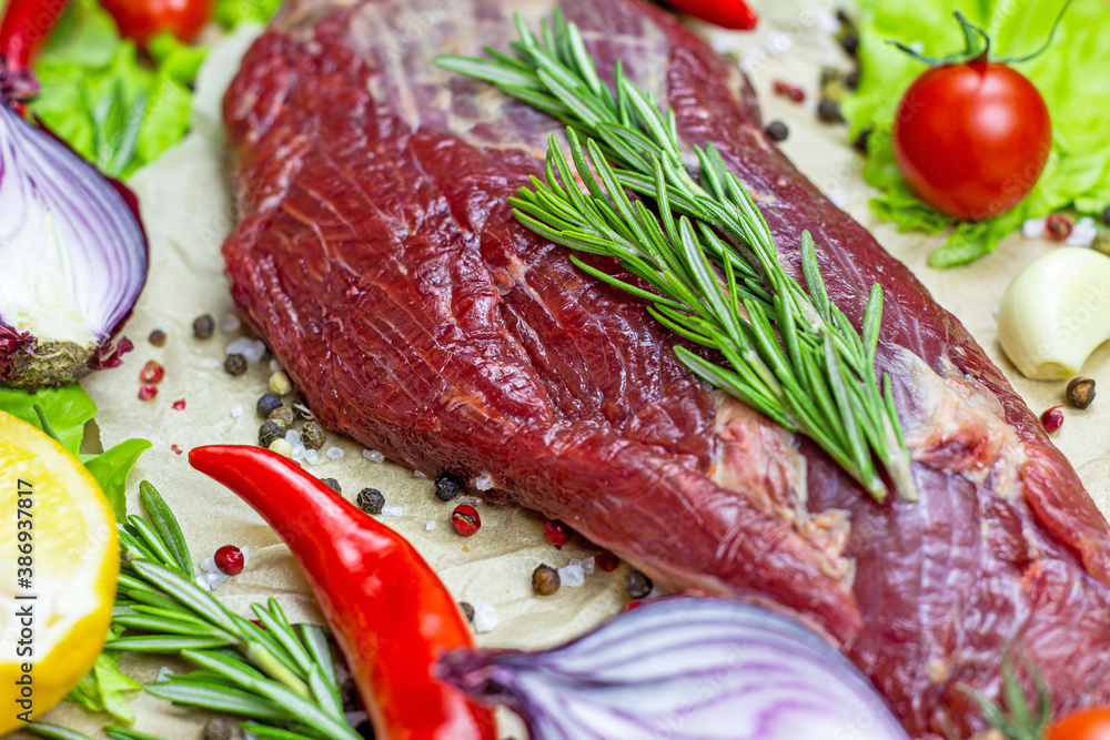 Raw red beef meat with green rosemary and fresh vegetables on light wooden cutting board background. Raw red beef meat with green rosemary and fresh vegetables on light wooden cutting board background.