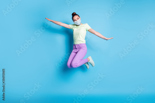 Fototapeta Naklejka Na Ścianę i Meble -  Full length photo of young girl jumping high keeping hands like plane wear mask isolated on vibrant blue color background