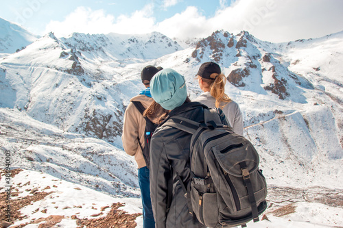 Three people in sports equipment stand on top of a snowy mountain.