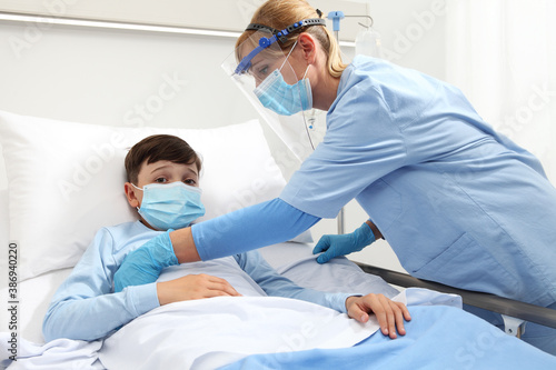 Nurse takes care of patient child in hospital bed, wearing protective visor mask, corona virus covid 19 protection concept 