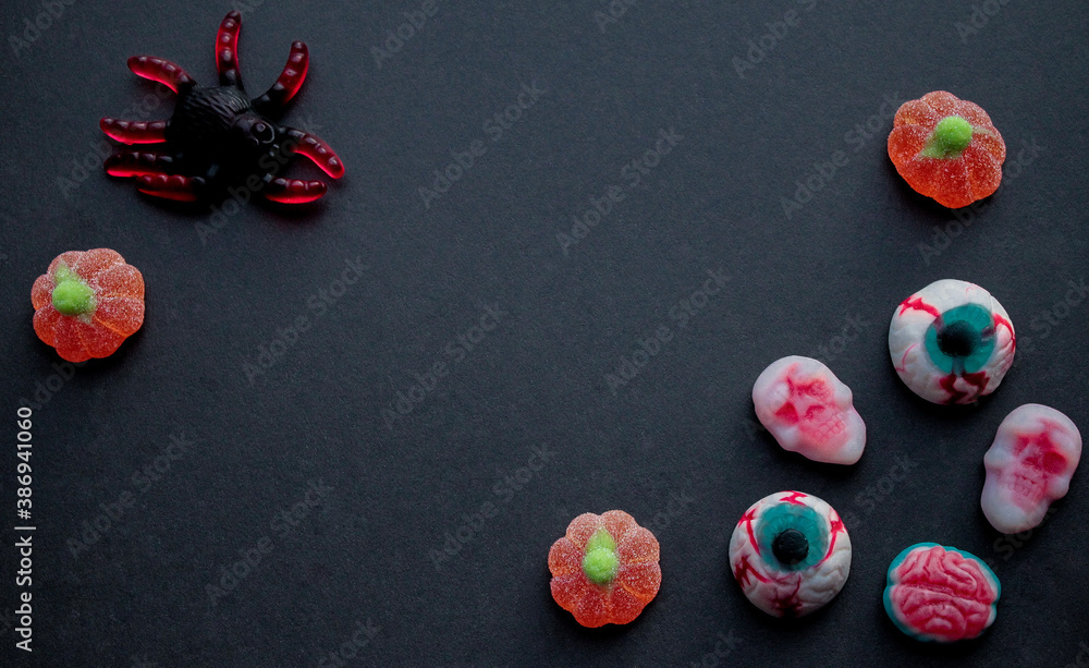 Halloween. Jelly candies in the form of huge black spider, orange pumpkins, skulls, eyes and brains on a black background. Copy space