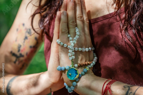 Female hands doing namaste mudra yoga practice in forest with mala necklace photo