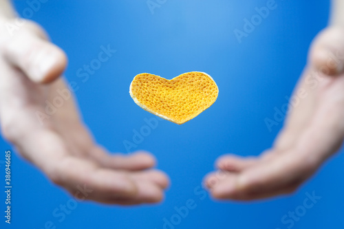 Heart shaped citrus peel and blurry hands on a blue background.