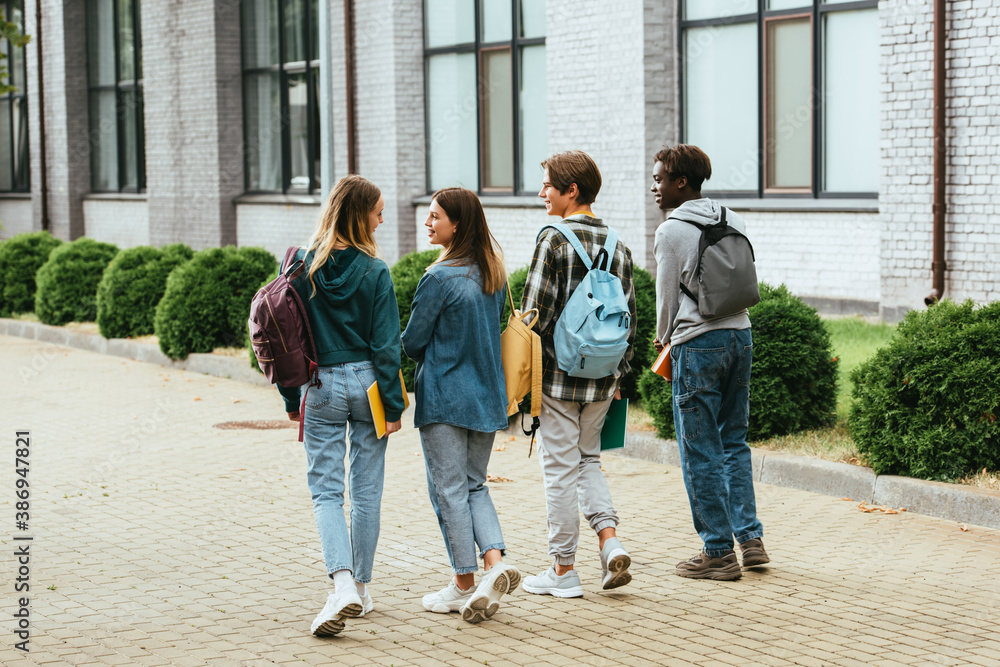 Back view of smiling teenagers with backpacks walking on urban street Back view of smiling teenagers with backpacks walking on urban street