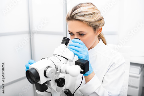 Portrait positive gynecologist woman sitting near a colposcope in her gynecological office. Gynecologist profession. Women's health photo