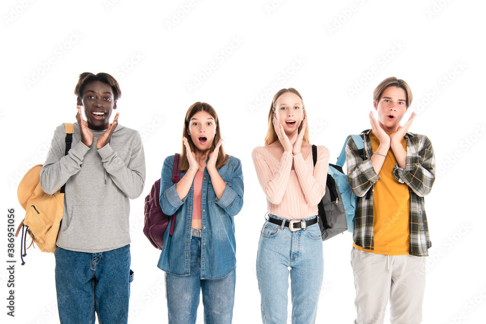 Shocked multiethnic teenagers with backpacks looking at camera isolated on white Shocked multiethnic teenagers with backpacks looking at camera isolated on white