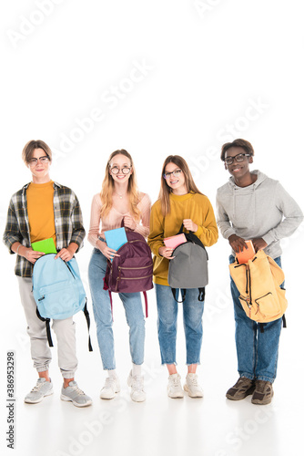 Cheerful multicultural teenagers with books and backpacks looking at camera on white background