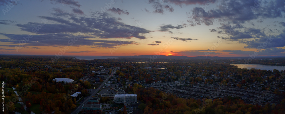 Aerial panoramic view of a golden sunset with clouds over the city of Laval showing the lake and mountains