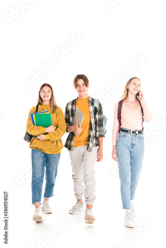 Smiling teenagers with backpacks, notebooks and smartphone walking on white background