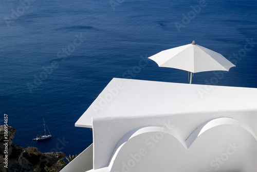 White building and white umbrella on a background of blue sea. Santorini. Greece.