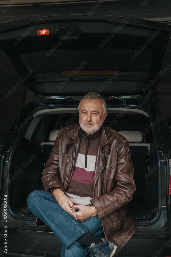 Handsome elderly man sitting in open trunk of car Handsome elderly man sitting in open trunk of car