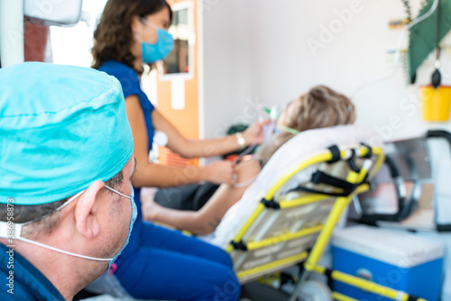 Female nurse paramedic with face mask helping a patient with respiratory system in ambulance during pandemic