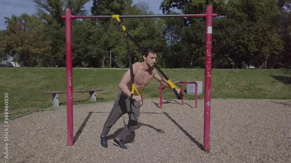 Young fit man doing TRX chest push, attractive confident male athlete working out outdoors Young fit man doing TRX chest push, attractive confident male athlete working out outdoors