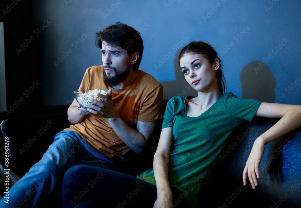 emotional woman and man with a plate of popcorn watching tv in the evening indoors