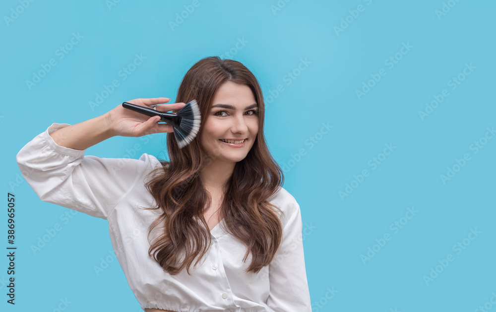 Beautiful young makeup artist on a blue background with a paintbrush smiling. Beautiful young makeup artist on a blue background with a paintbrush smiling.