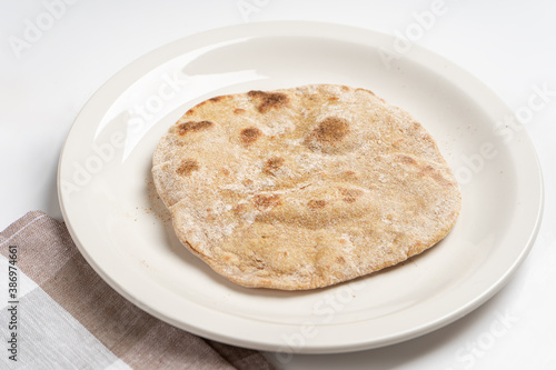 A flatbread on a white plate next to a napkin on the table