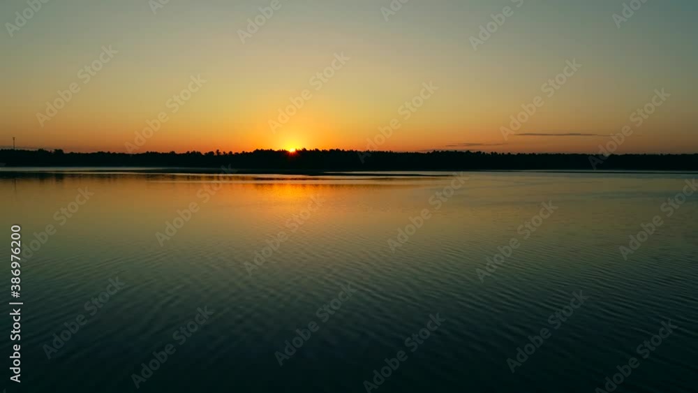 Aerial flight backwards over lake reveals rising sun over silhouetted treetops. Aerial flight backwards over lake reveals rising sun over silhouetted treetops.