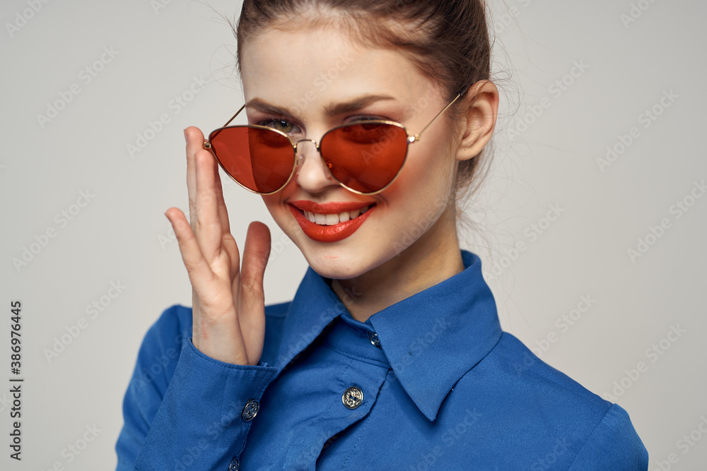 Fashionable woman in sunglasses and a blue shirt gesturing with her hands on a light background cropped view Fashionable woman in sunglasses and a blue shirt gesturing with her hands on a light background cropped view