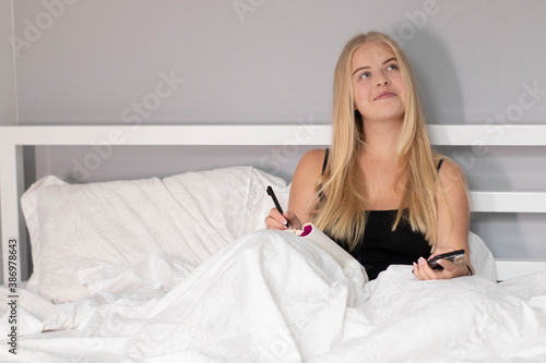 pensive thoughtful blonde on white bed with phone. pretty people on isolation.