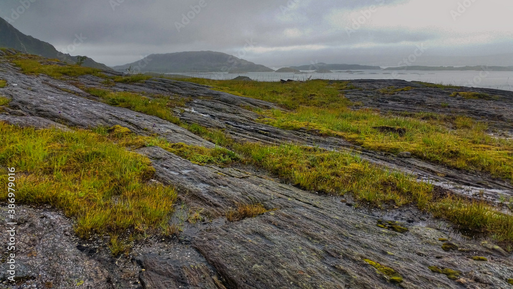 View to hiking trail to Dønnamannen peak going upwards a grey stone mountain slope covered by grass and moss in the Dønna island	