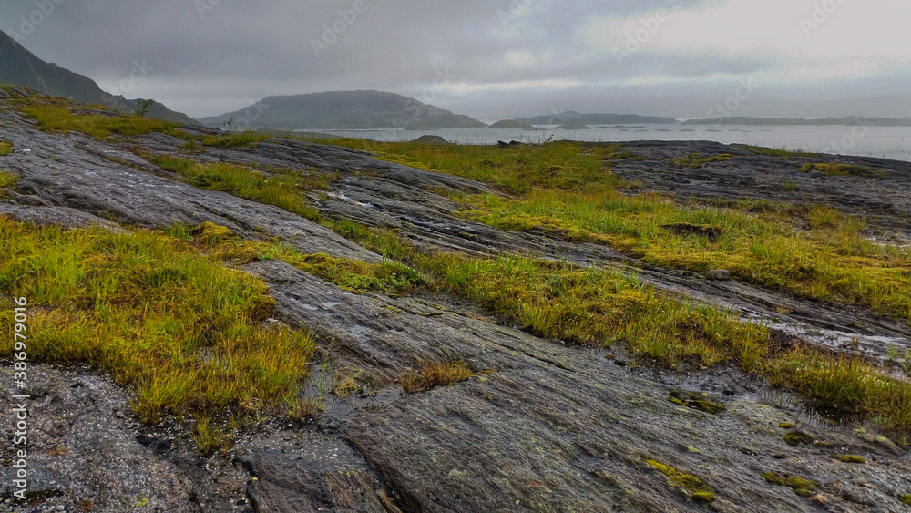 View to hiking trail to Dønnamannen peak going upwards a grey stone mountain slope covered by grass and moss in the Dønna island View to hiking trail to Dønnamannen peak going upwards a grey stone mountain slope covered by grass and moss in the Dønna island