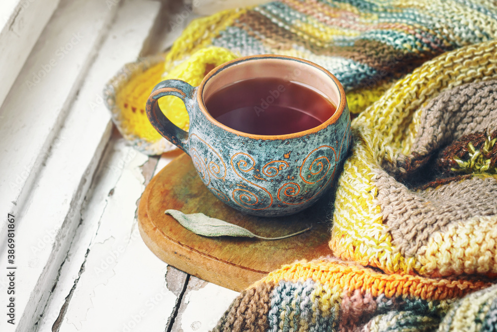 Cup of black tea, leaf of sage and knitted blanket on the windowsill. Cup of black tea, leaf of sage and knitted blanket on the windowsill.