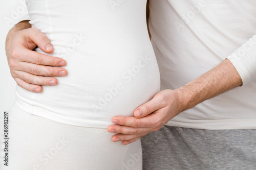 Young man hands hugging and touching pregnant woman belly. Emotional loving pregnancy time - 20 weeks. Baby expectation. Happiness and safety concept. Front side view. Closeup. © fotoduets