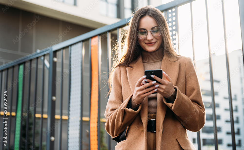 Fototapeta premium Businesswoman looking at her mobile phone while walking to office in the morning. Woman walking on city street to office using her mobile phone.