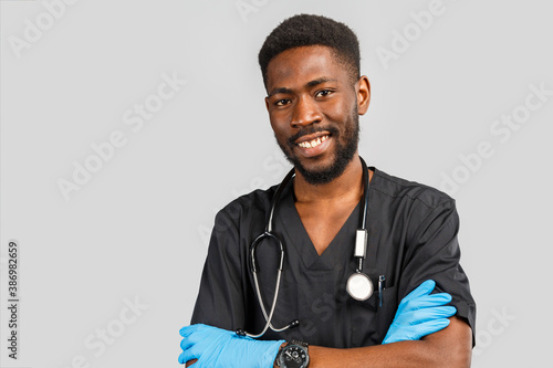young african or afro american doctor or surgeon with stethoscope and blue gloves standing against gray background © Nana_studio